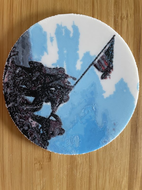 A round coaster printed with the Iwo Jima flag raising in blue, white and dark tones, on a wooden table