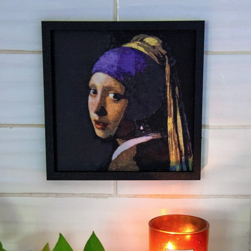 A framed Girl with a Pearl Earring print on a tiled wall above a lit candle
