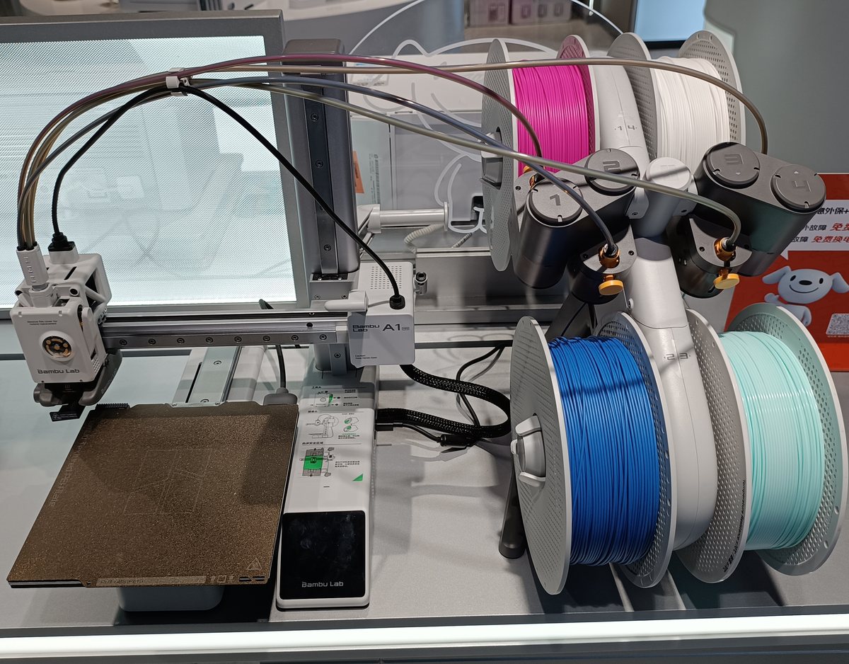 A Bambu Lab A1 mini printer with an AMS lite holding four spools beside it