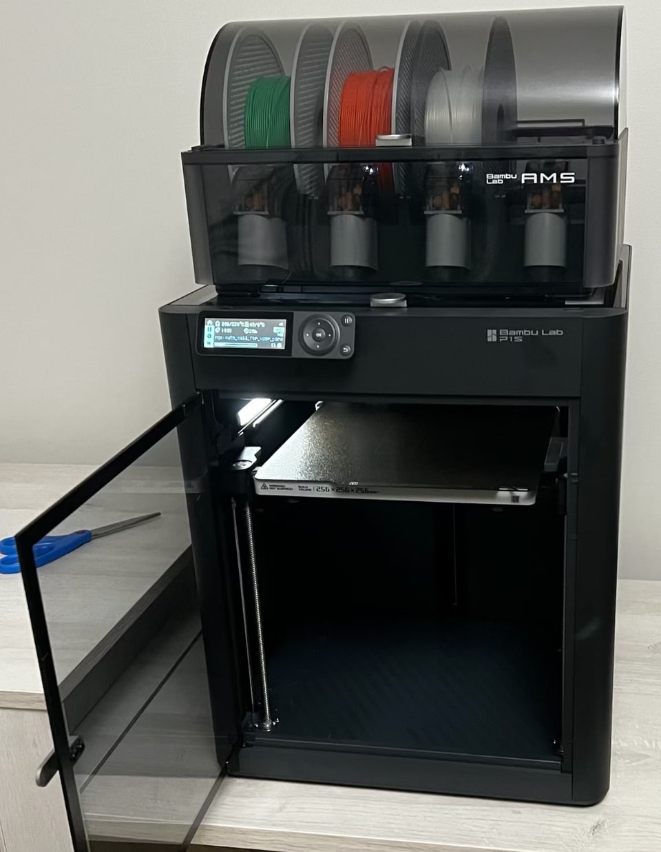 A black Bambu Lab P1S printer with its door open and an AMS on top