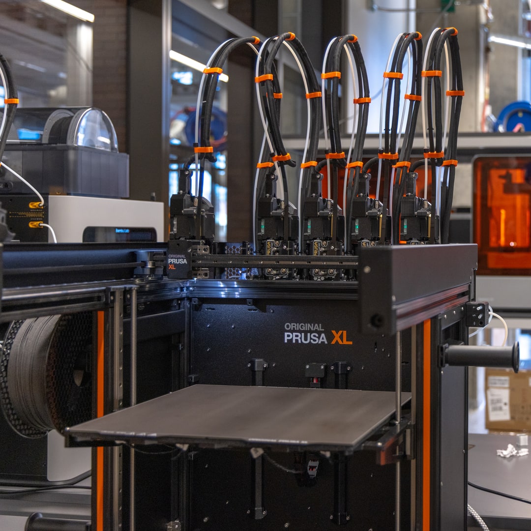 A Prusa XL printer with five toolheads and their filament tubes above the print bed