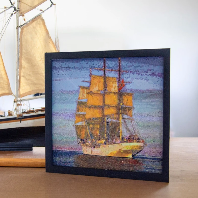 A framed print of a tall ship beside a model sailing ship on a shelf