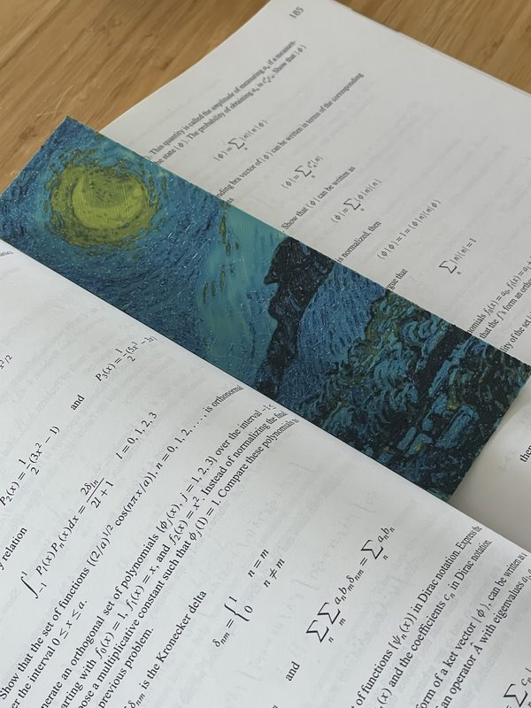 A Starry Night bookmark with raised brush strokes, lying across an open physics textbook