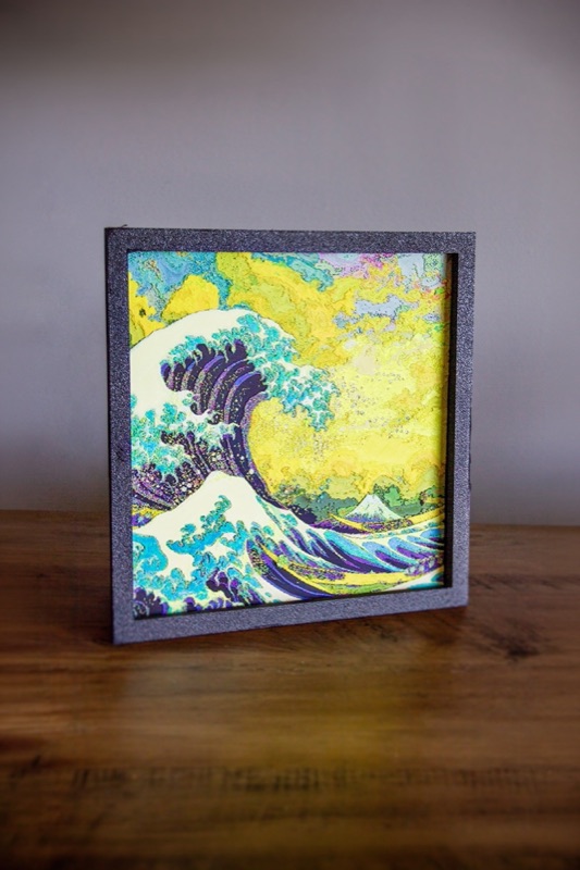 A framed relief print of The Great Wave standing on a wooden table